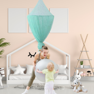 Dans un coin de jeu, maman joue au ballon son enfant, derrière elle est accrochée un ciel de lit bébé.