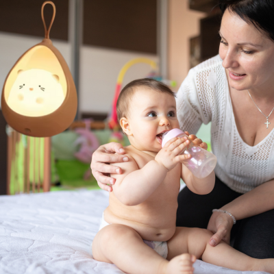 Maman tient son enfant sur un lit regarde qu'il soit apaiser et avec un biberon dans mains. 