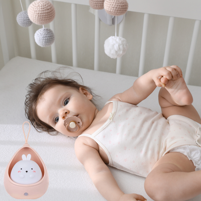 Dans un berceau, un enfant allongé observe avec appréciation veilleuse bébé.