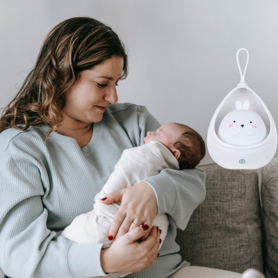 Maman assis dans son canapé admire son enfant dans ses bras avec veilleuse bébé avec un bon moment.  