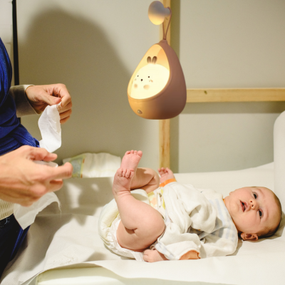Maman change son enfant avec un appui-utile sur la table à langer éclairée par une veilleuse bébé. 